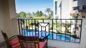 A balcony with a view of a swimming pool, surrounded by greenery and a building.