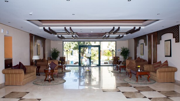 A spacious lobby with a checkered floor, two sofas, a coffee table, and a glass door leading outside.