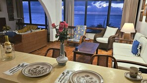 Una habitación con vista al océano, un comedor con platos y cubiertos, y mobiliario de mimbre.