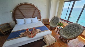 Un dormitorio amplio con una cama grande, vista al océano y un balcón con una silla y una mesa.