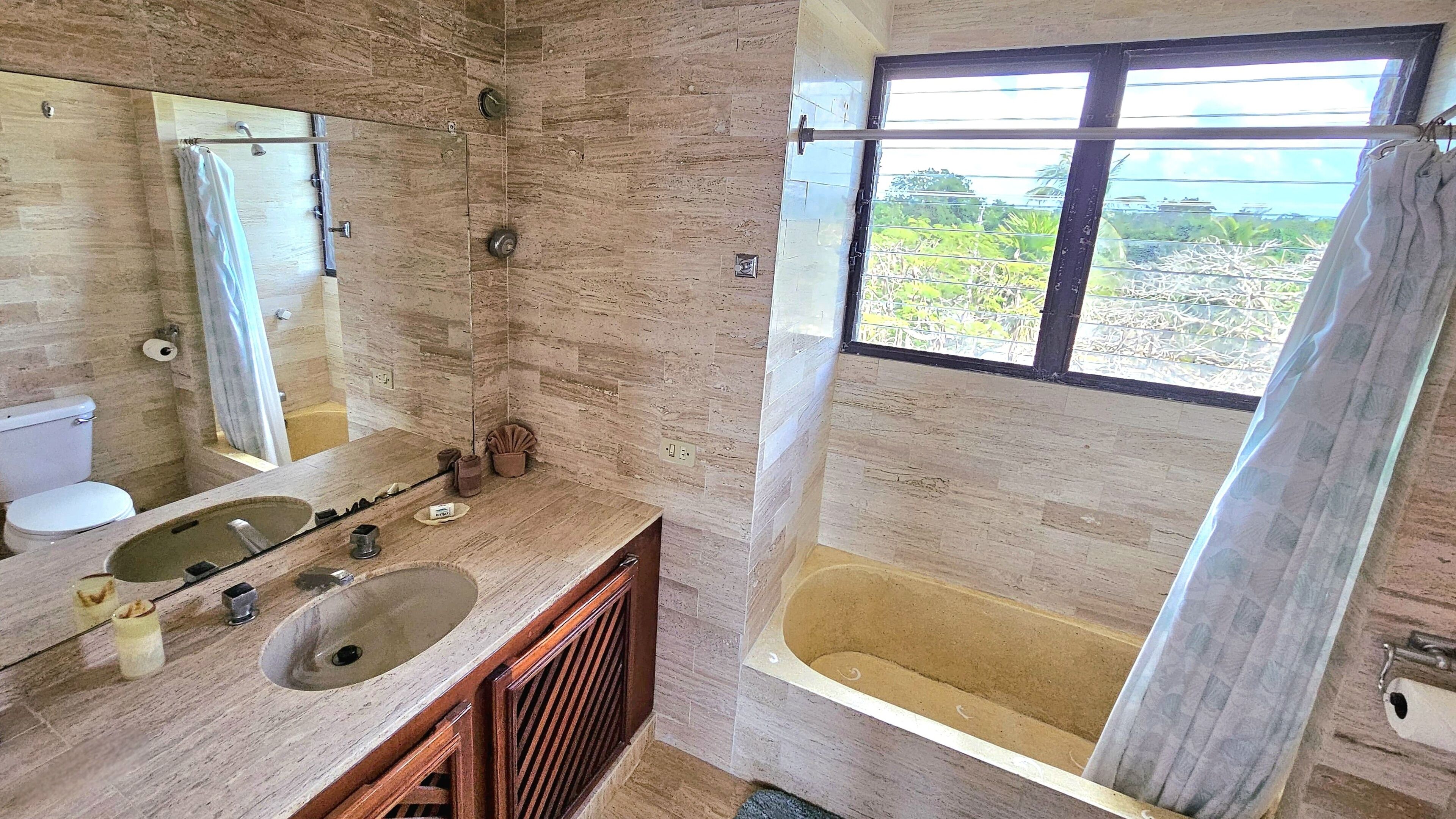 A bathroom with a bathtub, a large mirror, a toilet, and a sink.