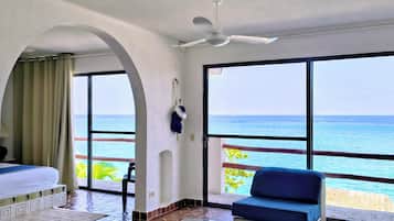 A hotel room with a balcony, a bed, a sofa, a table, and a view of the ocean.