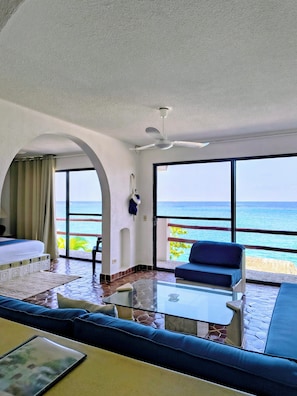 Een hotelkamer met balkon, een bed, een bank, een tafel en uitzicht op zee.