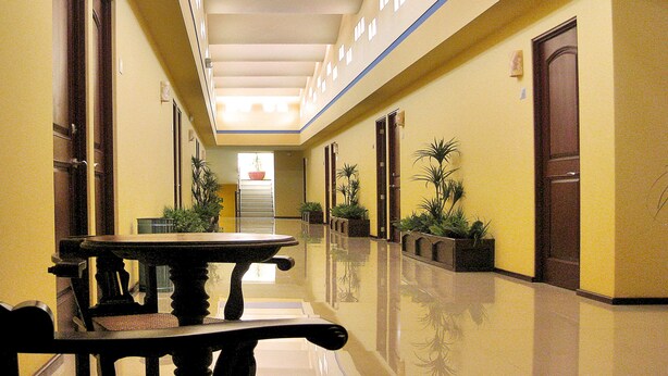 Un pasillo de hotel con una larga mesa y sillas, plantas en macetas y puertas a ambos lados.