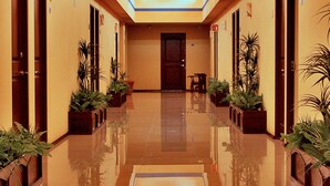Un pasillo de hotel con suelo reflectante, plantas en macetas y puertas a ambos lados.