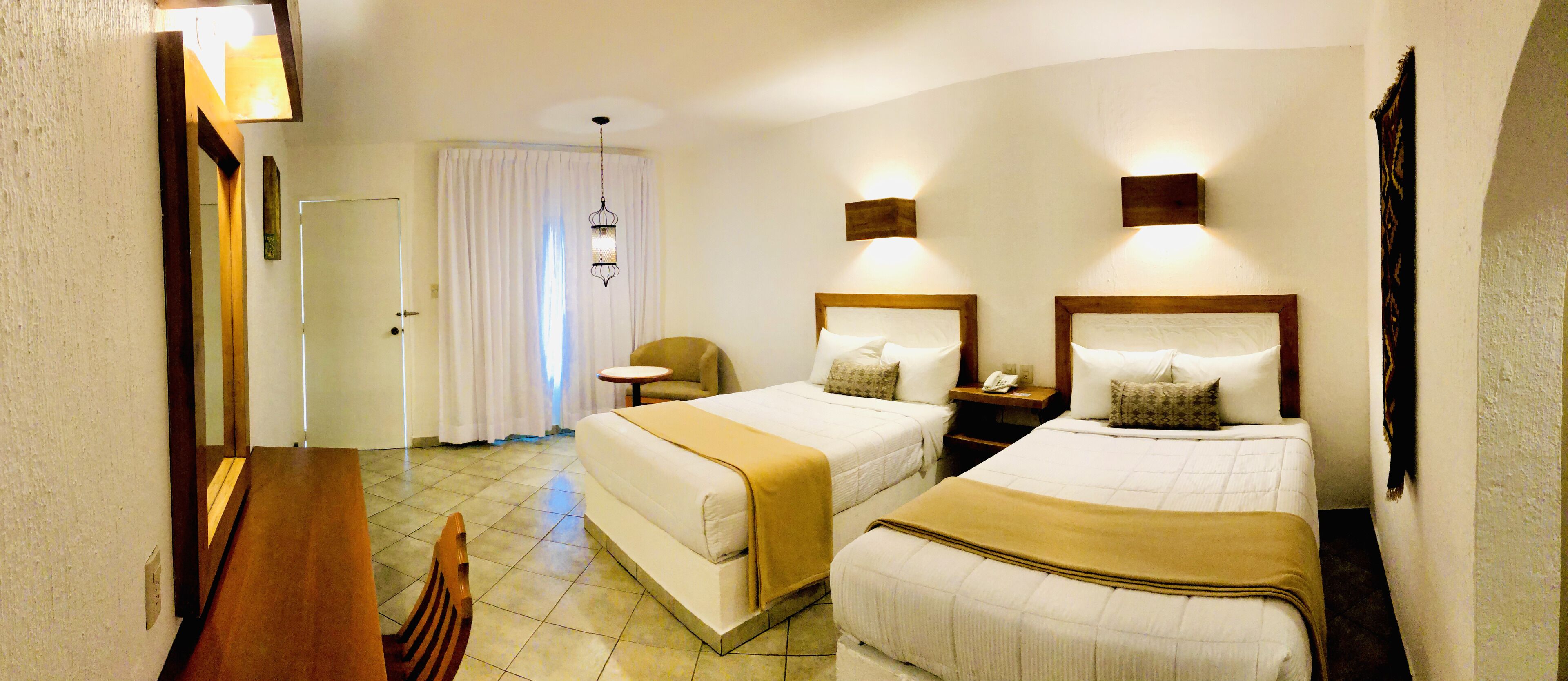 A hotel room with two beds, a small table, a chair, a nightstand, and a mirror.