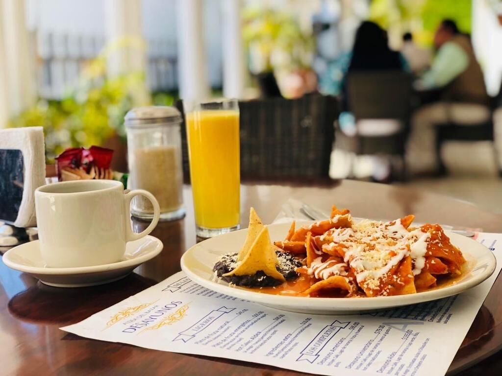 Una mesa de comedor con un plato de enchiladas, un vaso de jugo de naranja y una taza de café.