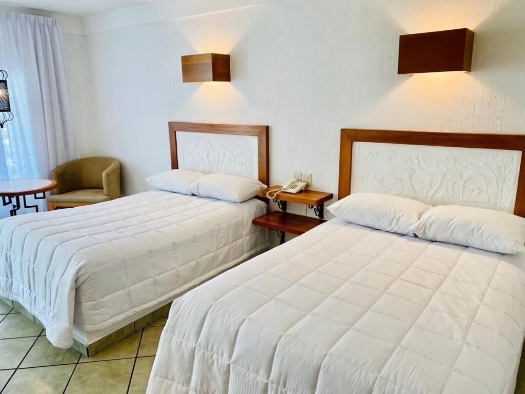 A hotel room with two beds, a small table, and a chair.