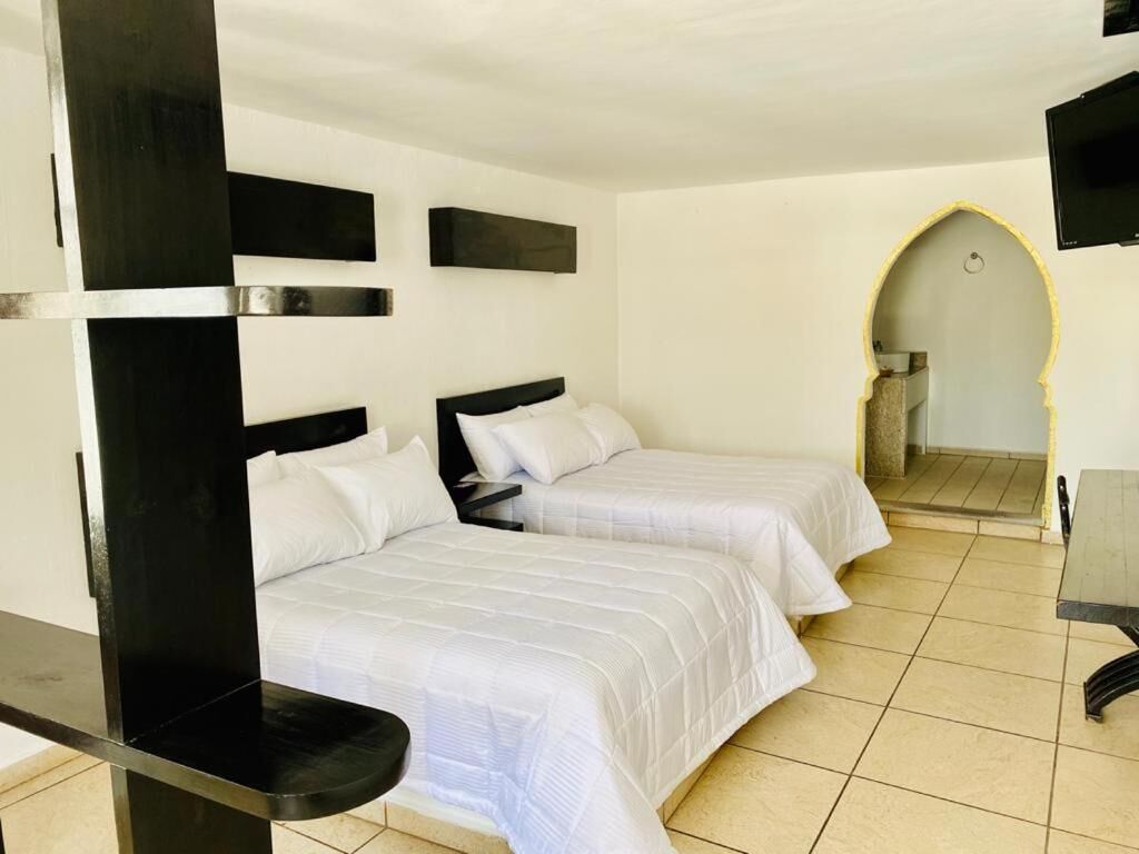 A hotel room with two beds, a TV, and a bathroom visible through an arched doorway.
