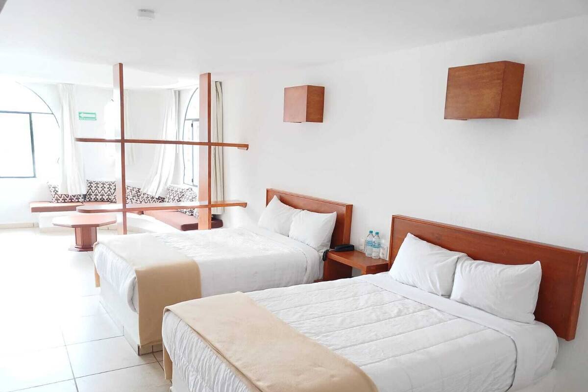 A hotel room with two beds, a sitting area with a sofa and chairs, and a large window.