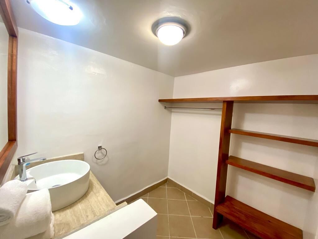 A bathroom with a white sink, a towel, a wooden shelf, and a ceiling light.