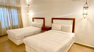 Habitación de hotel con dos camas individuales, una mesita de noche, una lámpara y una ventana con cortinas.