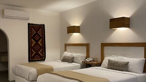 A hotel room with two beds, a patterned rug, a wall-mounted air conditioner, and two wall sconces. - Aldea del Bazar (Tehuacán)