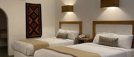 Une chambre d’hôtel avec deux lits, un tapis à motifs, un climatiseur fixé au mur et deux appliques murales.