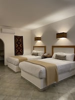 Ein Hotelzimmer mit zwei Betten, einem gemusterten Teppich, einer Wandklimaanlage und zwei Wandleuchten.