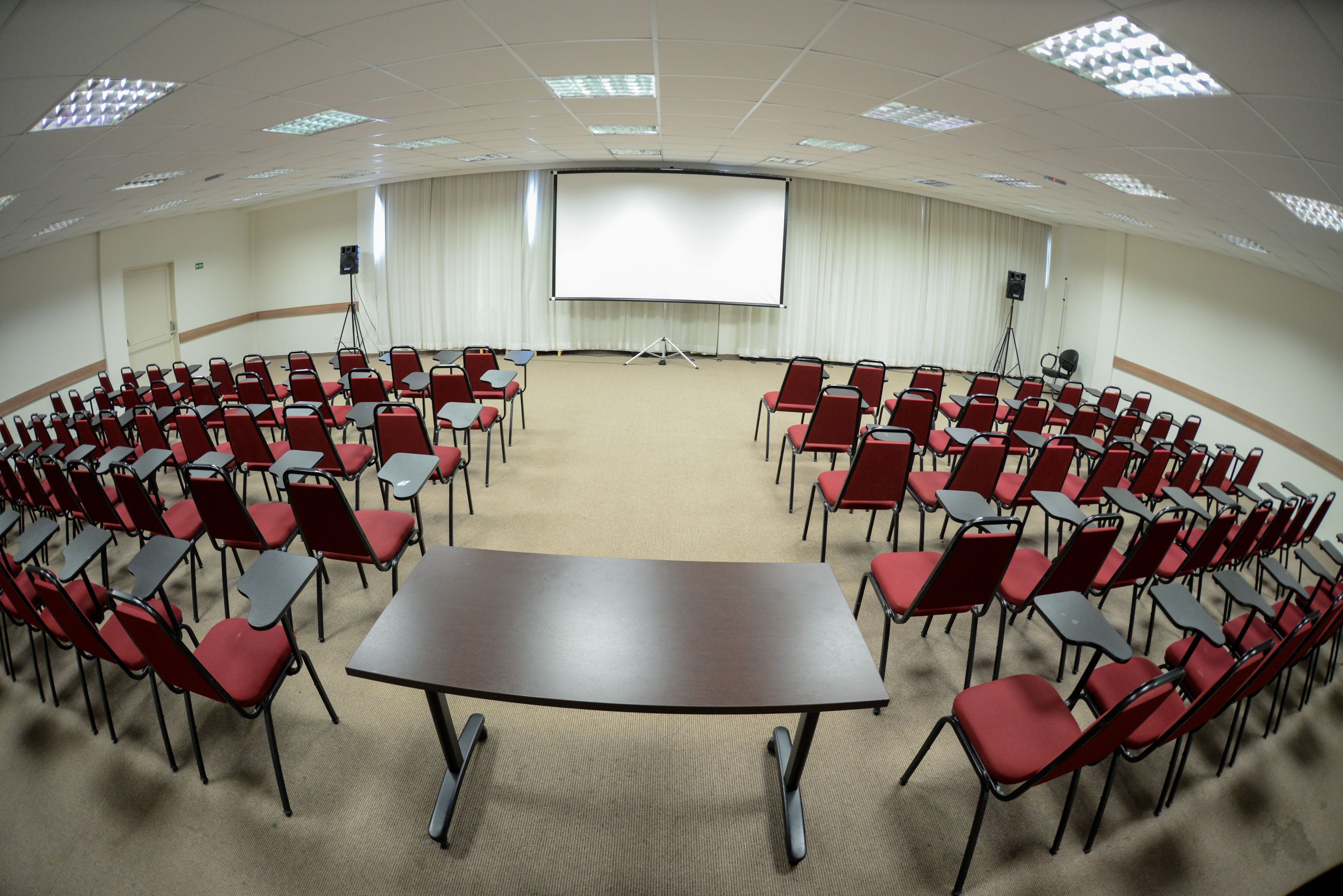 Ein Konferenzraum mit einem großen Tisch, roten Stühlen, einer Projektionsleinwand und einem Teppichboden.