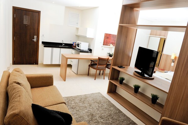 Un espace de vie compact comprenant un canapé, un téléviseur posé sur un meuble en bois, une table à manger avec des chaises, un coin cuisine avec un four à micro-ondes et une porte.
