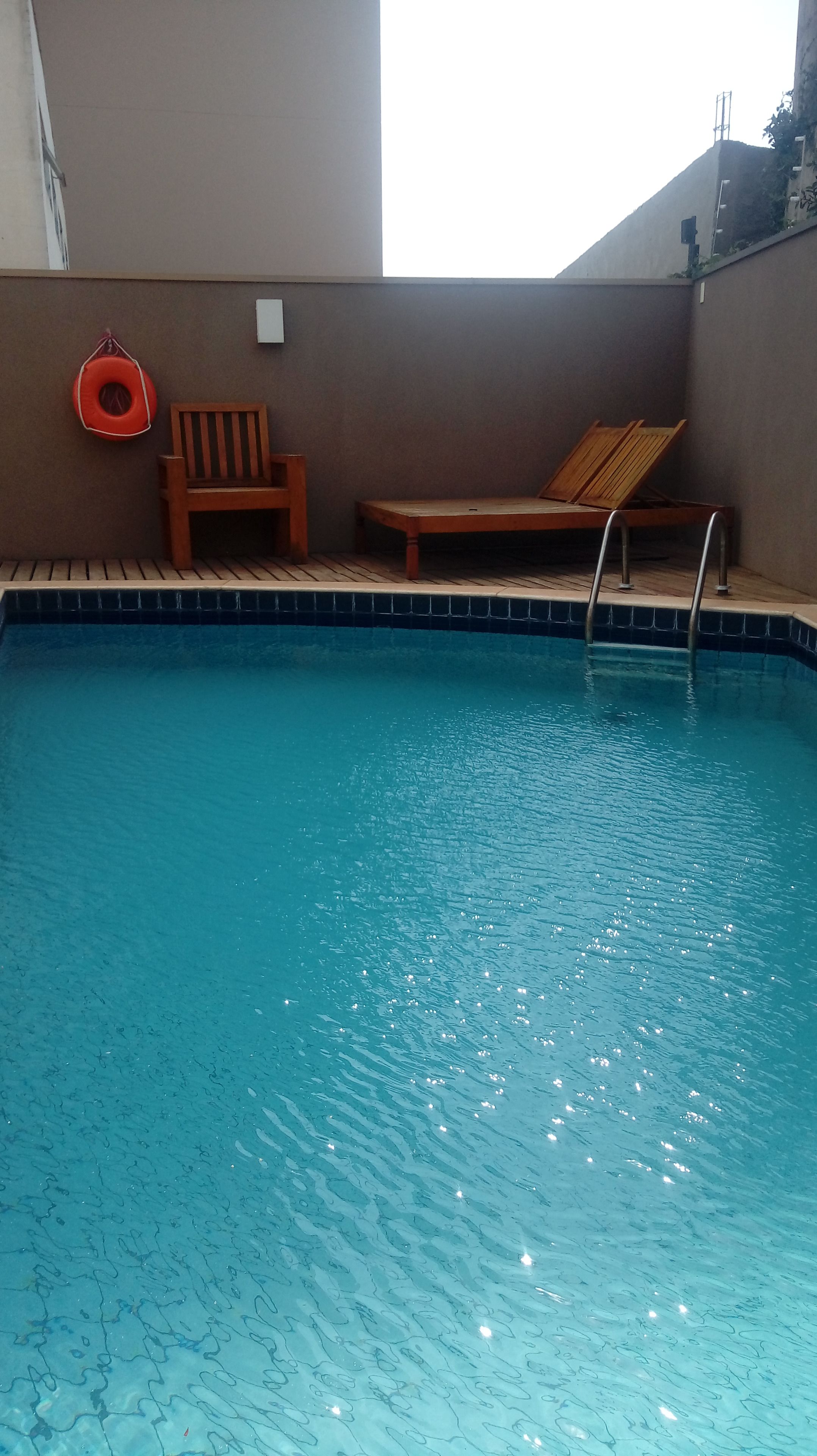 Una piscina con muelle de madera, un flotador salvavidas y un banco.