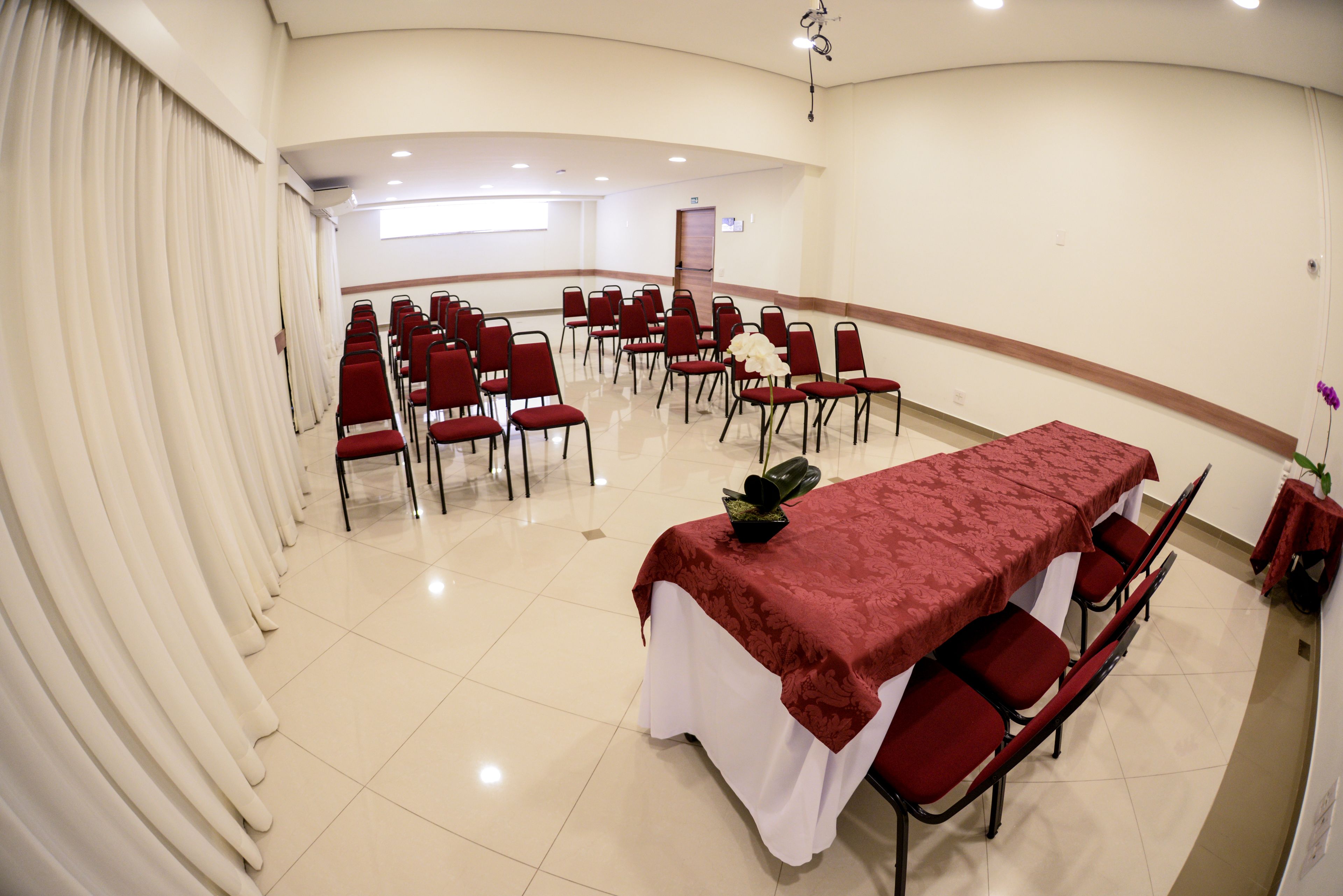 A conference room with a long table, red chairs, and a white curtain.