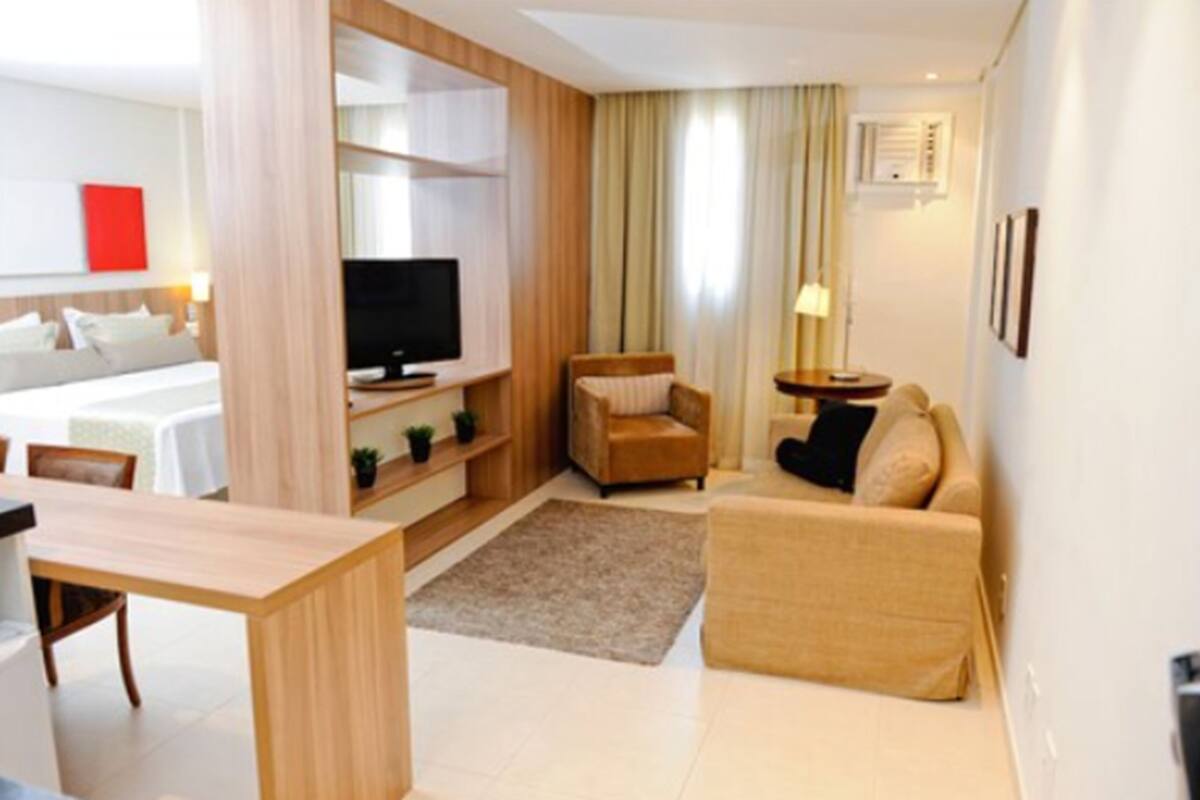 A modern hotel room with a bed, a TV, a sofa, a small table, and a desk.