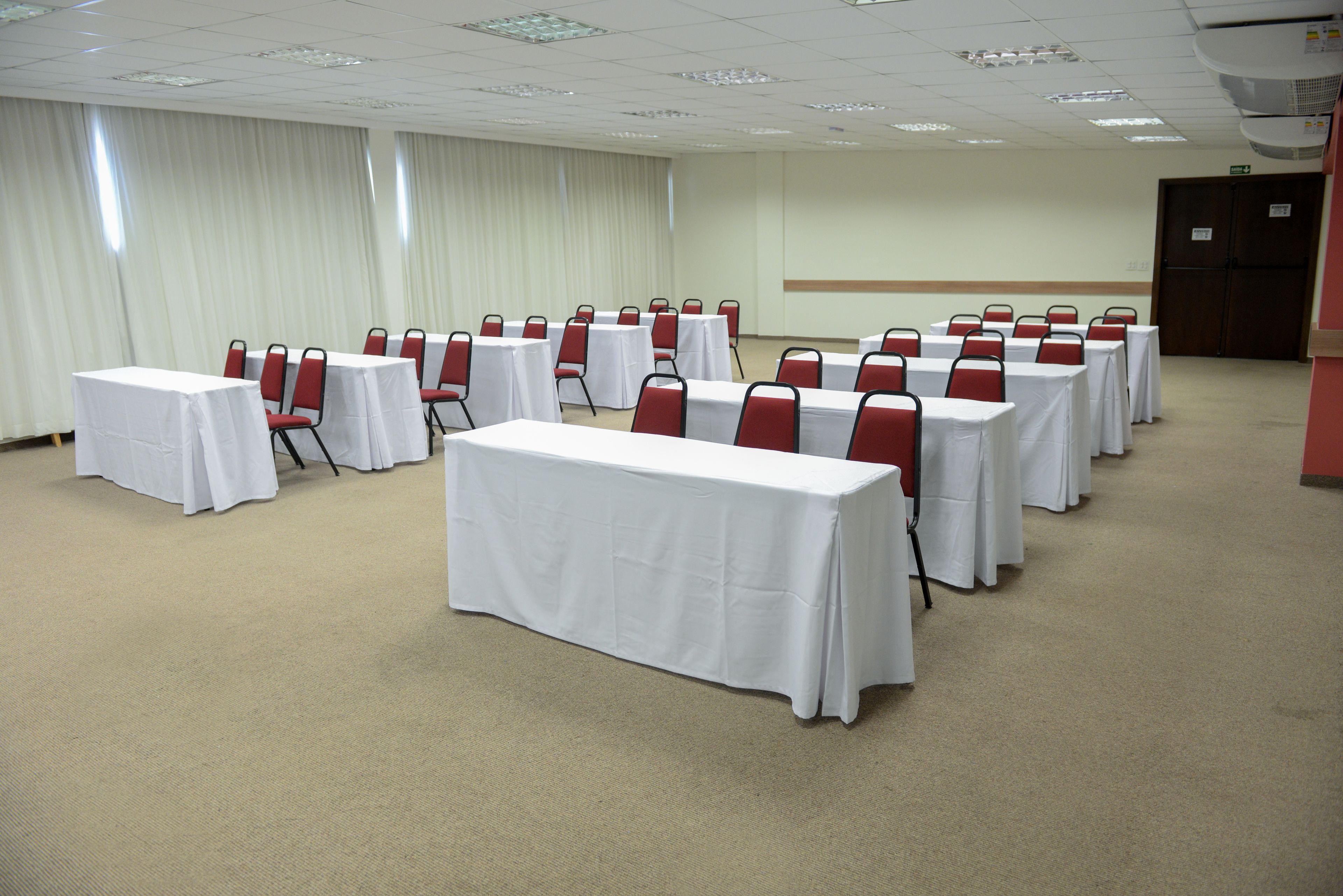 A conference room with rows of tables and chairs, a white carpet, and a door in the background.