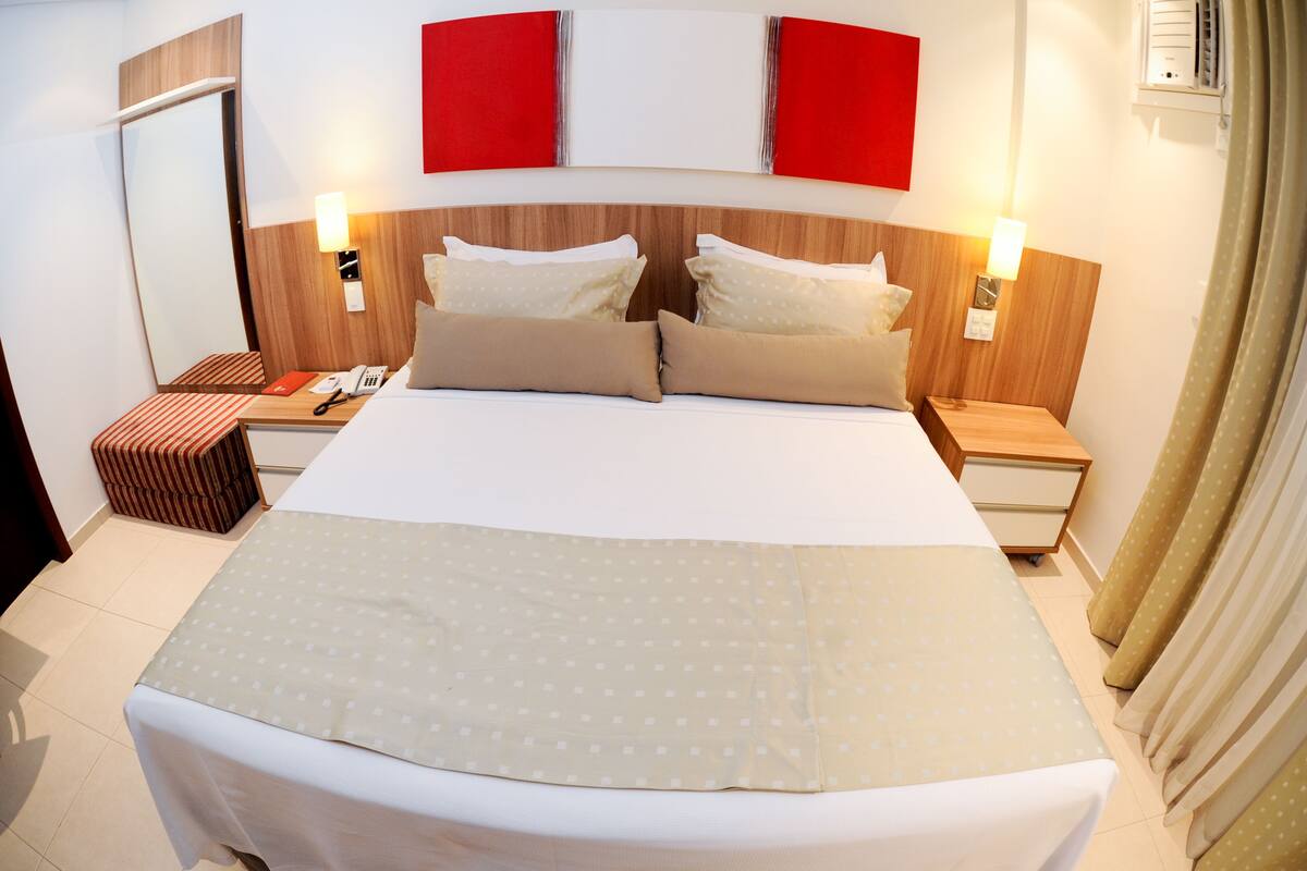 A hotel room with a large bed, two bedside tables, a nightstand, a mirror, and a red accent wall.