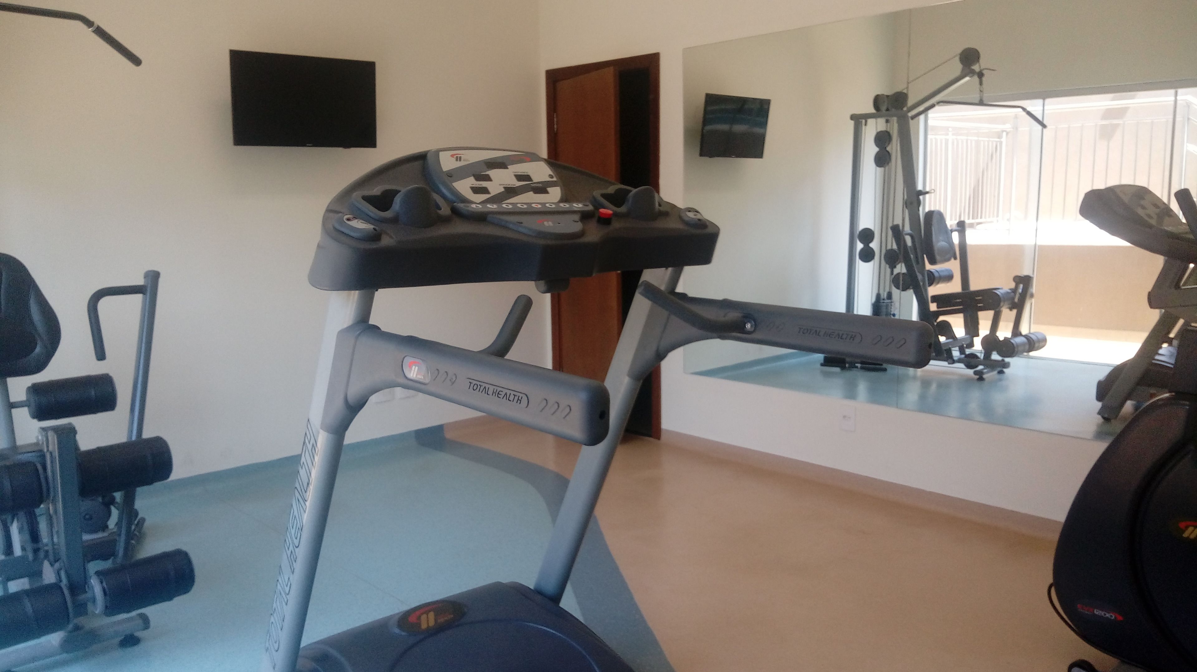 A gym with exercise equipment, including a treadmill, weights, and a mirror.