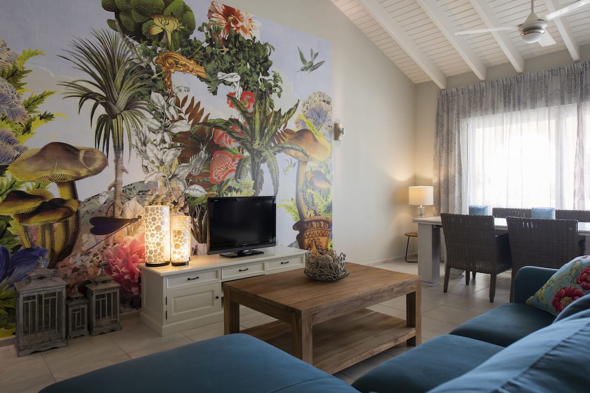 Una sala de estar con un gran mural floral, un televisor, una mesa de centro de madera y sofás azules.