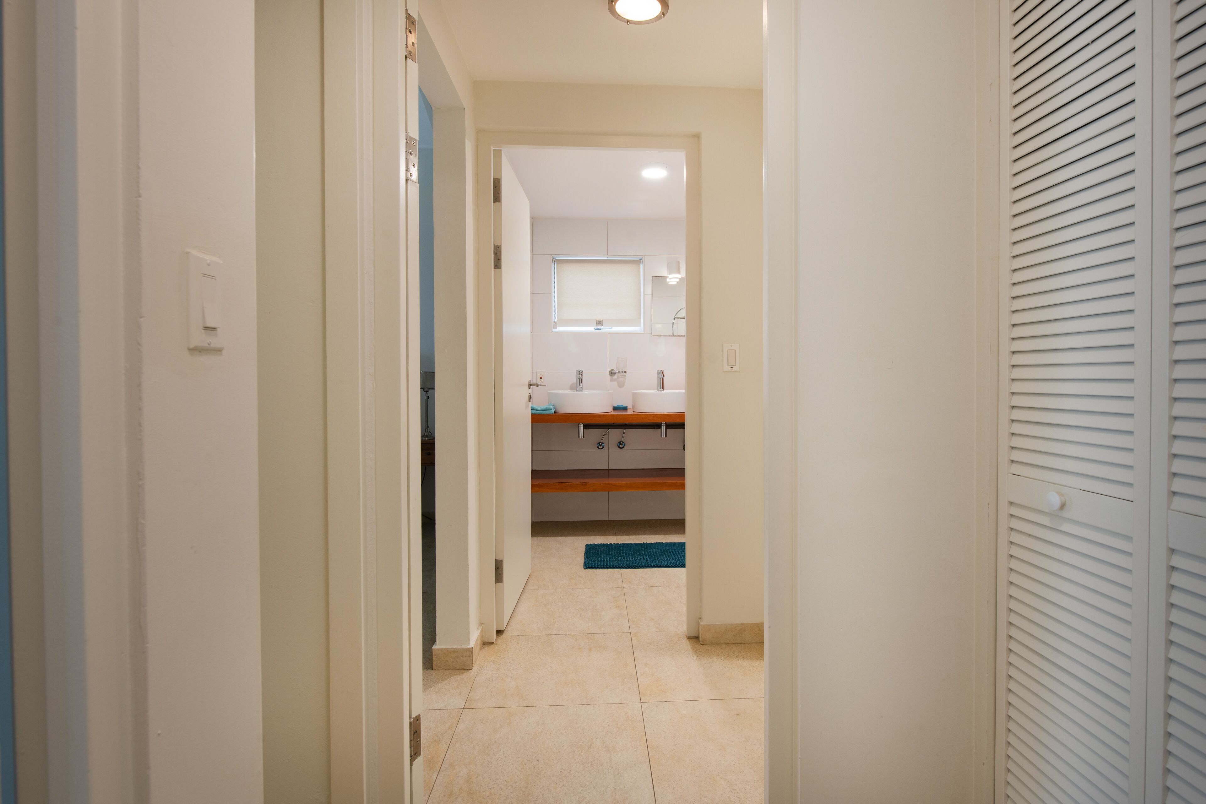A hallway leading to a bathroom with a sink and mirror.