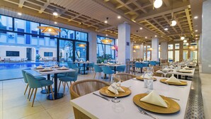 A restaurant with tables set for dining, large windows, and a pool area visible outside. - Presidente Beach (Salinas)