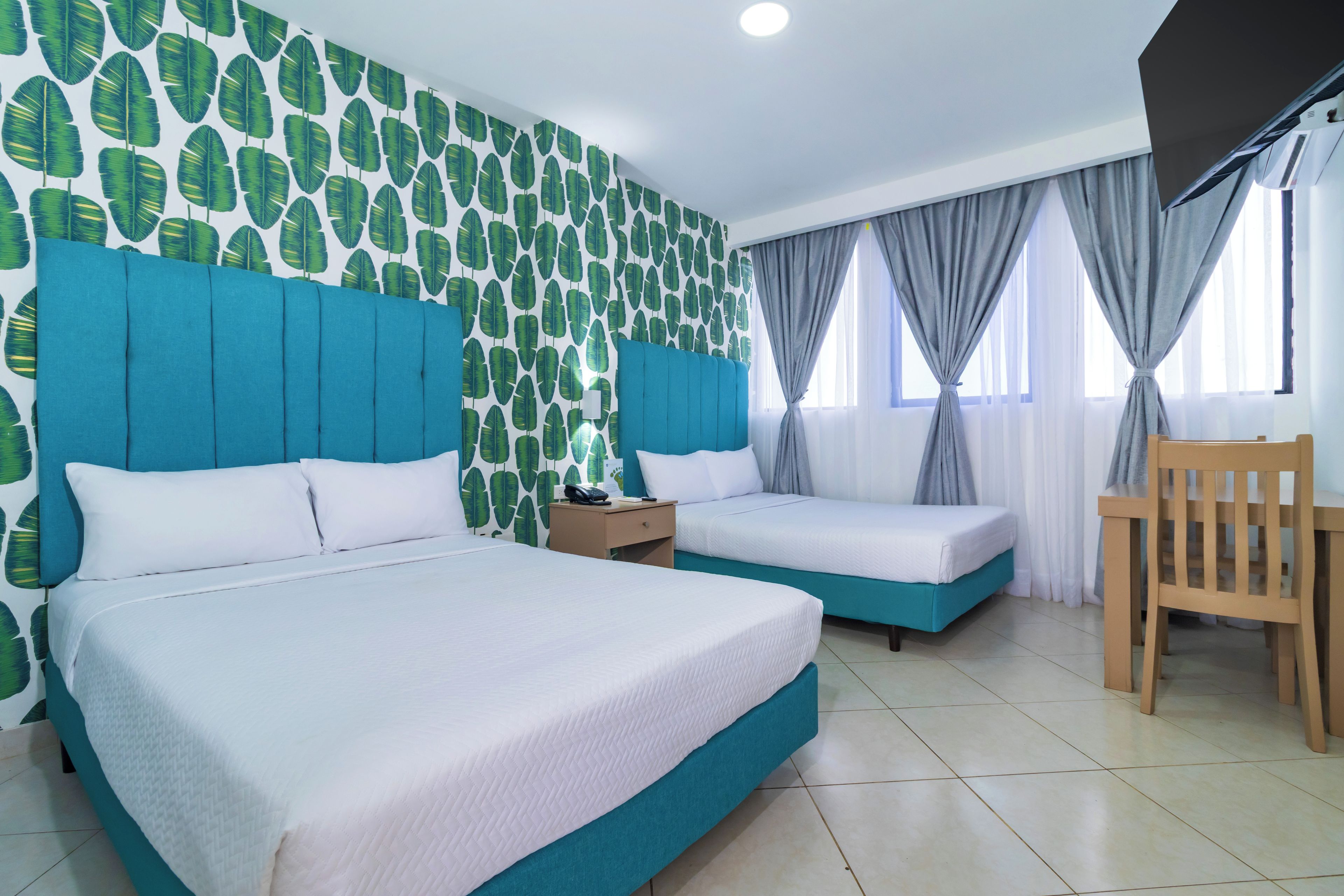 A hotel room with two beds, a wooden chair, a nightstand, and a wall with a leaf pattern.