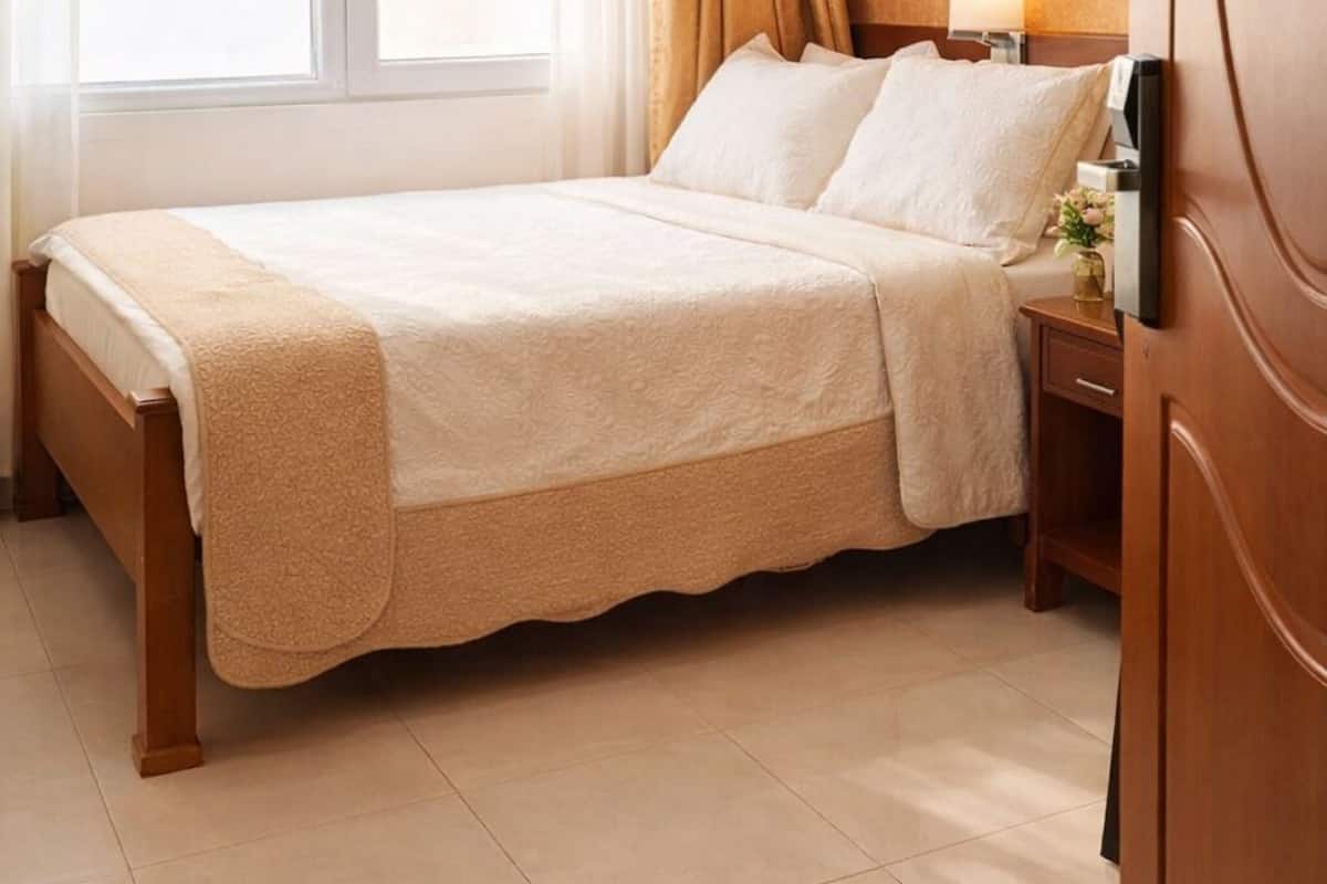 Una habitación de hotel con cama, mesita de noche, lámpara y ventana con cortinas.