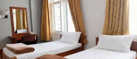 Habitación de hotel con dos camas de madera, un ventilador de techo, un aire acondicionado, un espejo y una ventana con cortinas.