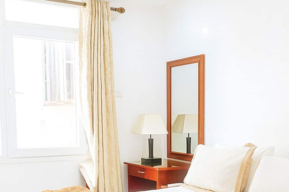 Una habitación de hotel con una cama grande, una mesita de noche de madera, un espejo, una lámpara y una ventana con cortinas.