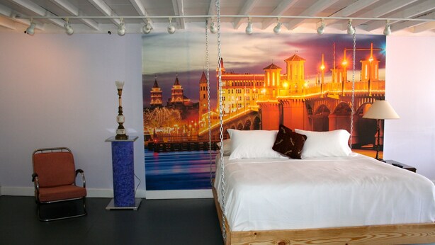 A bedroom with a bed, a chair, a desk, and a wall mural. - The Loft at Menorcan Square (St. Augustine)