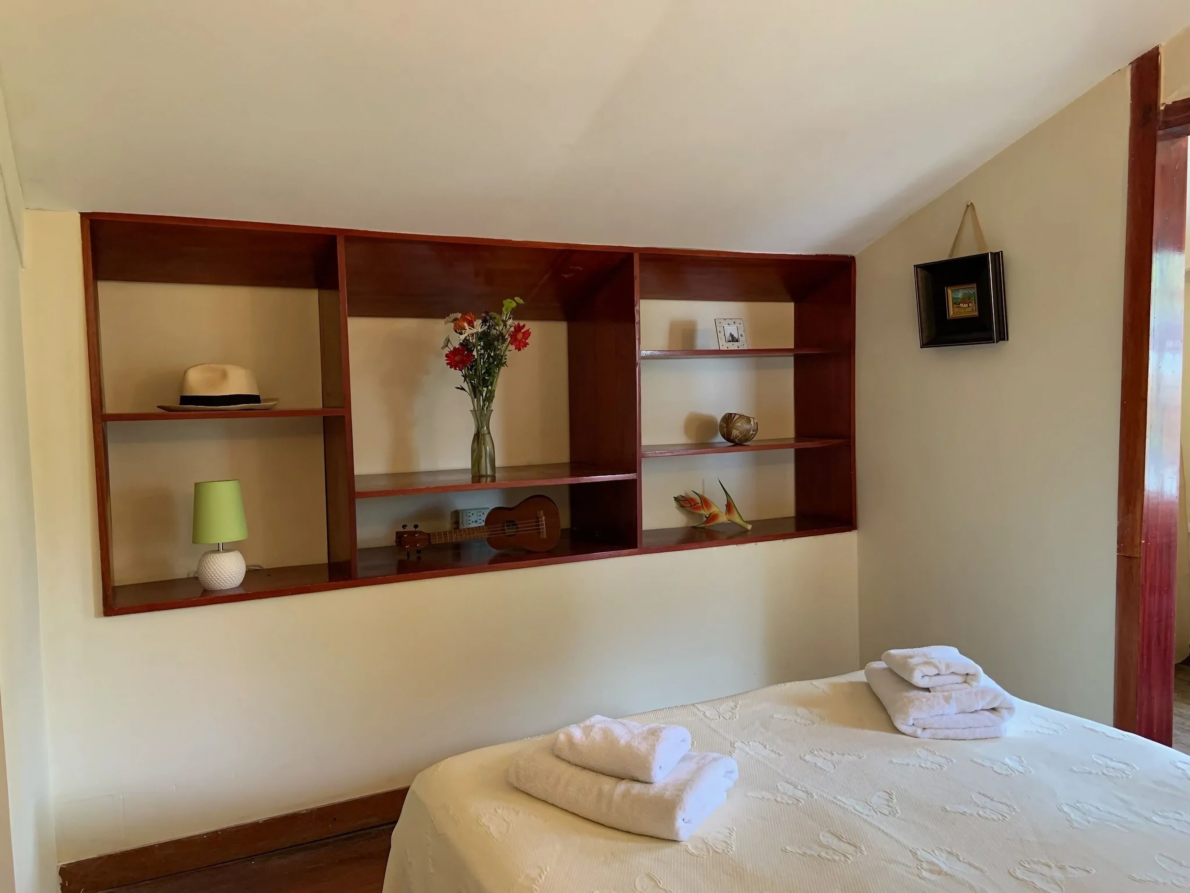 Una habitación de hotel con una cama grande, un aparador de madera con objetos decorativos y un cuadro en la pared.
