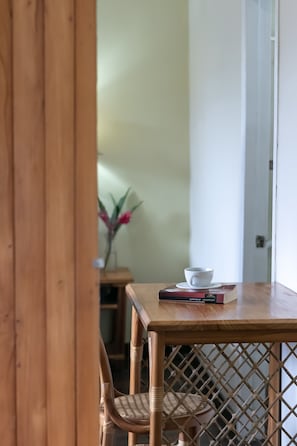 A wooden table with a white cup and a book, a wicker chair, and a lattice partition.