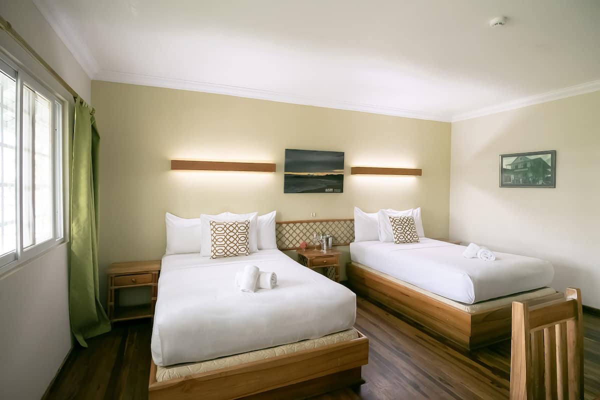 A hotel room with two beds, wooden headboards, a nightstand, a small table, and a window with curtains.