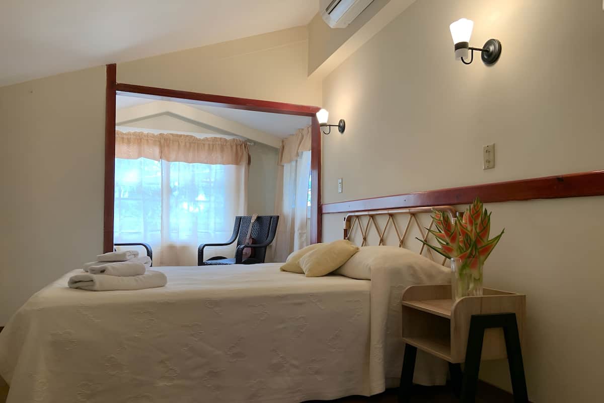 A neatly made bed with towels, a chair, and a small table with a plant.