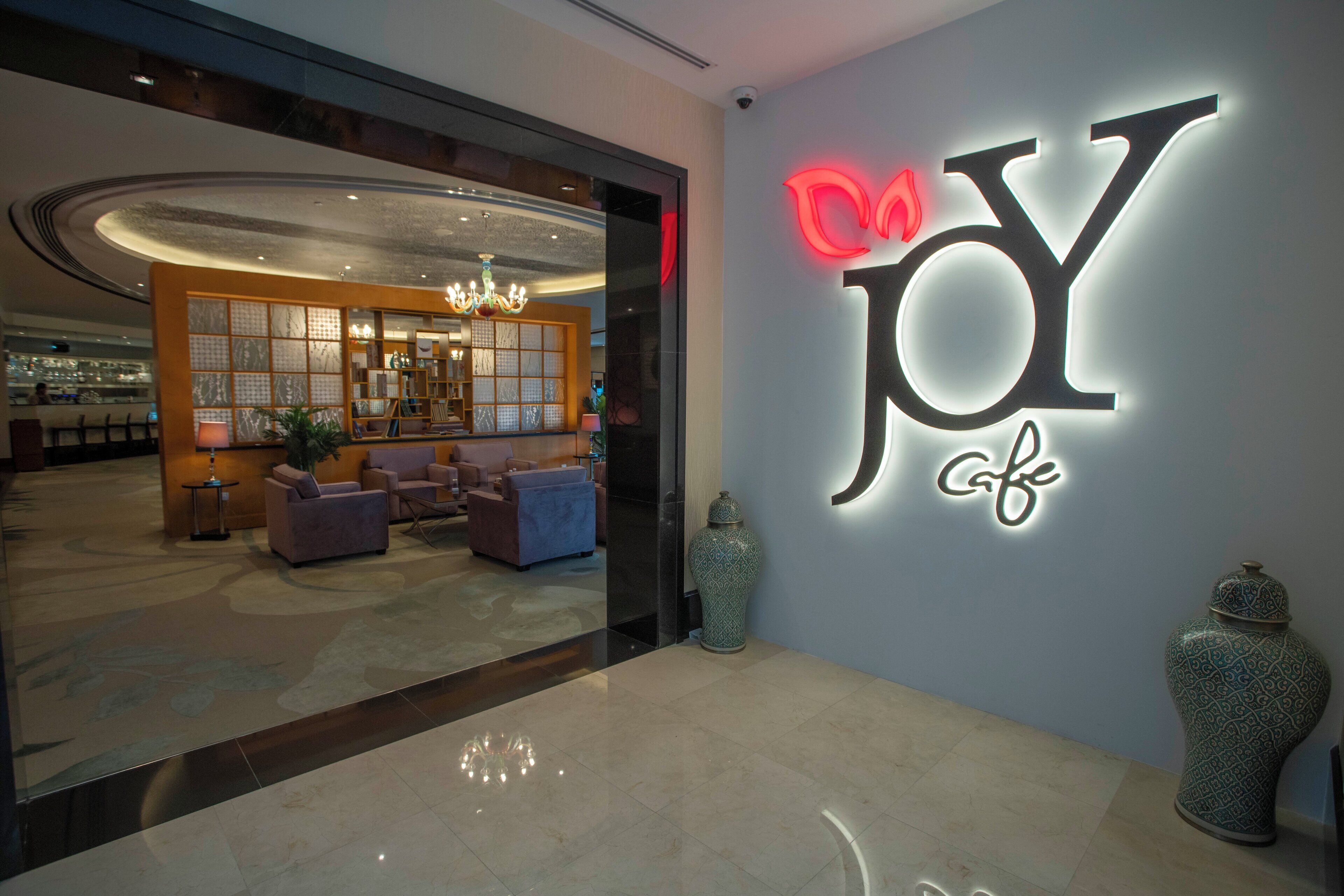 A modern interior with a reception area, seating, and a large illuminated sign reading "JOY cafe".