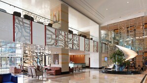 A spacious lobby with a modern design, featuring a central seating area with sofas and armchairs, a reception desk, and a glass staircase leading to upper levels. - Millennium Hotel and Convention Centre Kuwait (Salmiya)