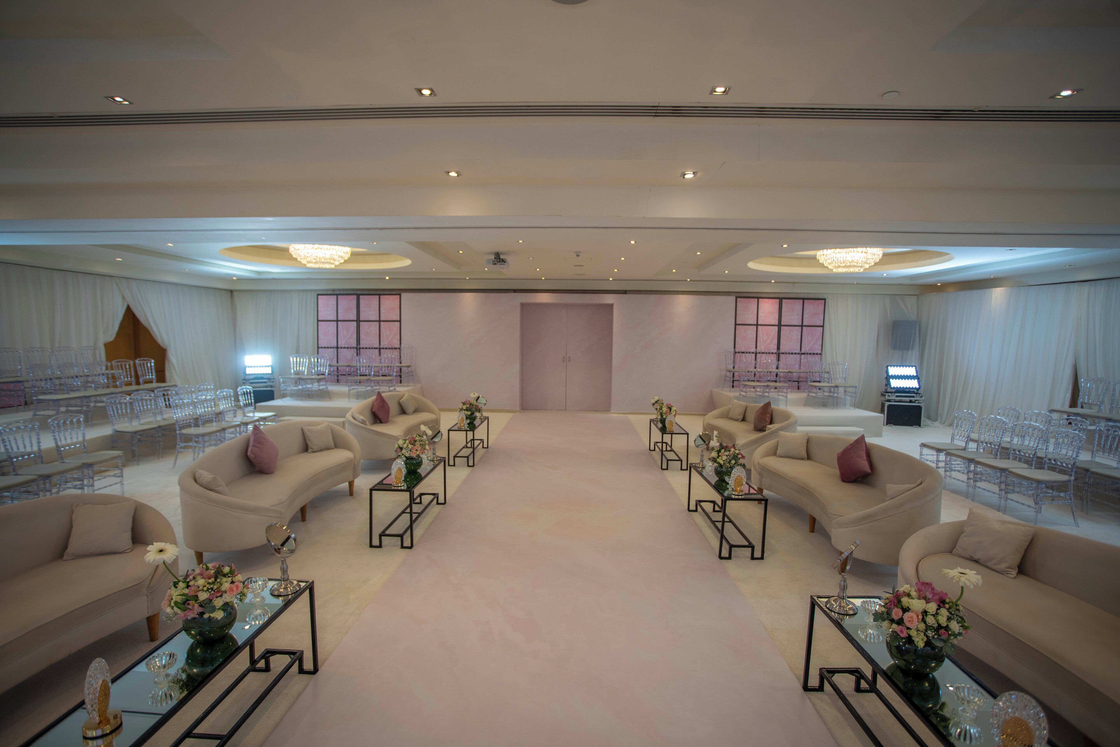 Un hall d’hôtel spacieux, doté de plusieurs espaces salon, d’une grande porte centrale et d’un lustre.