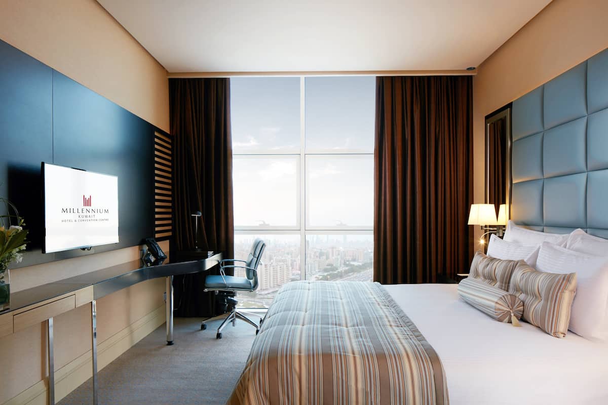 Une chambre d’hôtel équipée d’un lit, d’un bureau, d’une chaise, d’une télévision et d’une grande fenêtre avec des rideaux.