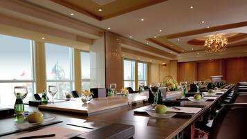 A conference room with a long table set for a meeting, equipped with chairs, a projector, and a large window offering a view of a cityscape.
