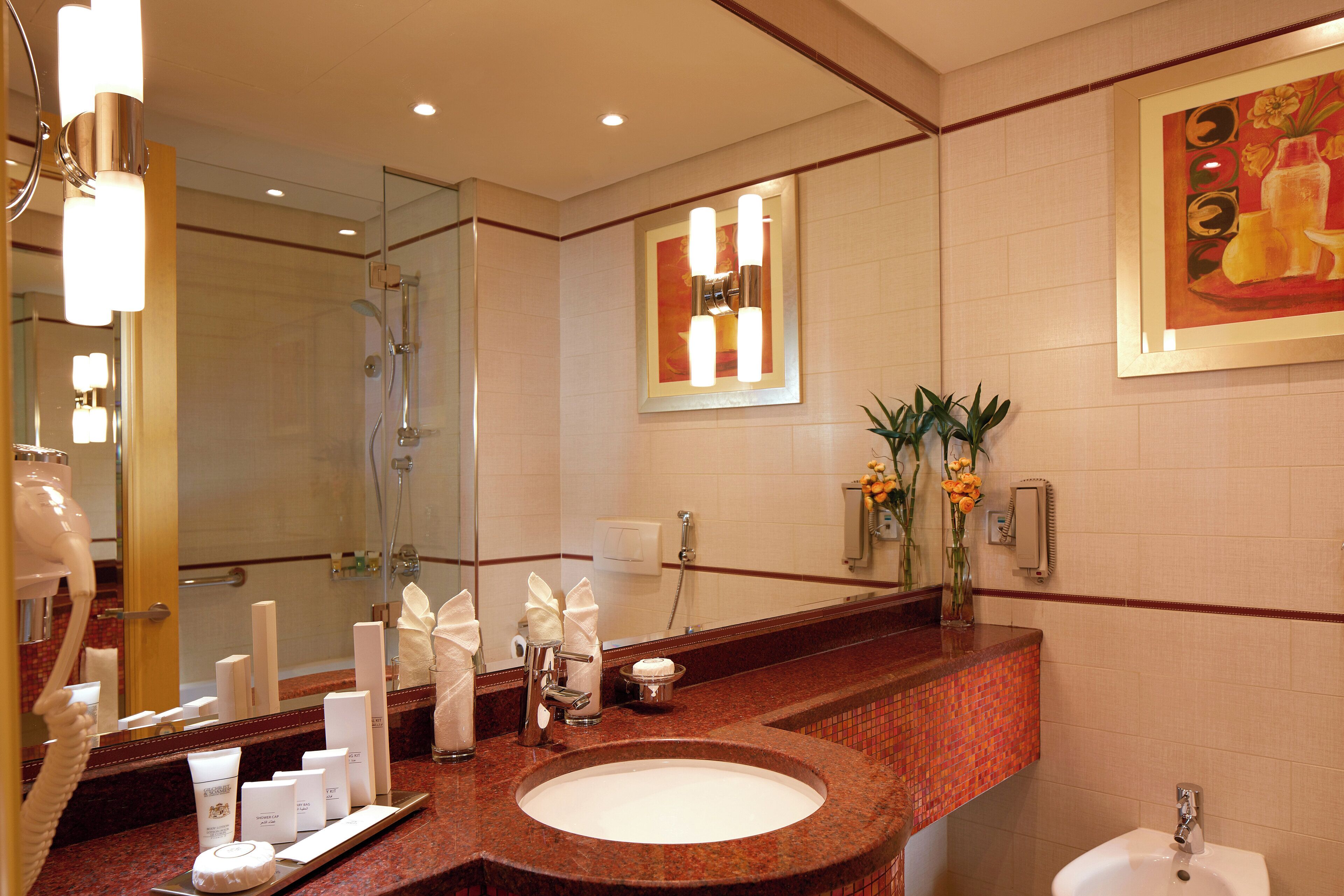A hotel bathroom with a marble sink, a large mirror, and a shower.
