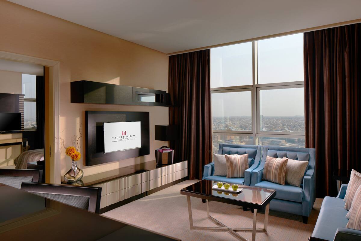 Une chambre d’hôtel moderne dotée d’une grande fenêtre, d’un téléviseur à écran plat, d’un canapé, d’une table basse et d’un coin repas.