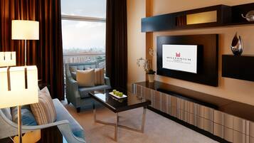 Een moderne hotelkamer met een grote televisie, een bank, een bijzettafeltje met appels en uitzicht op de stad.