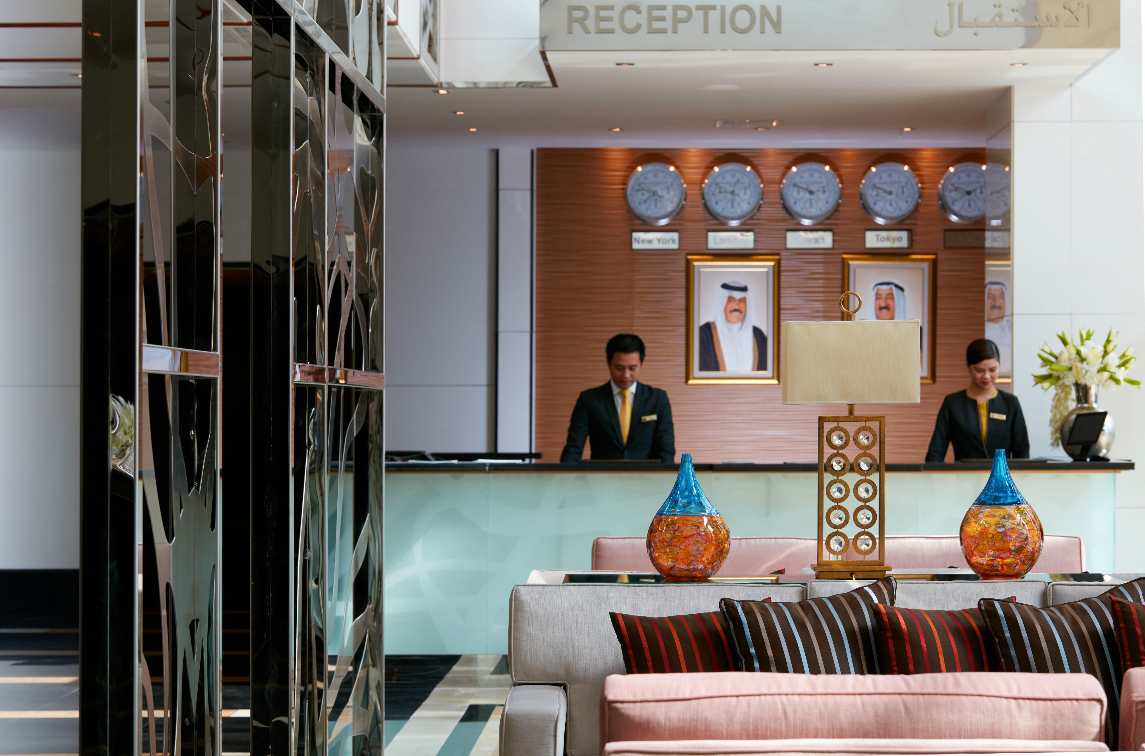 A reception area with a modern design, featuring a reception desk, two waitstaff, and a seating area with a sofa and decorative vases.