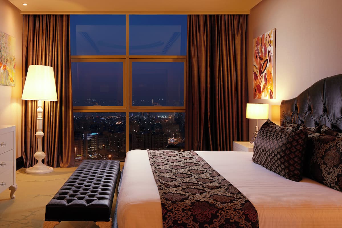 Une chambre d’hôtel avec une grande fenêtre, un lit, un banc et un téléviseur.
