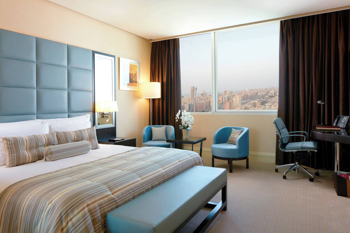 Une chambre d’hôtel avec un grand lit, un bureau, deux chaises et une vue sur le paysage urbain par la fenêtre.